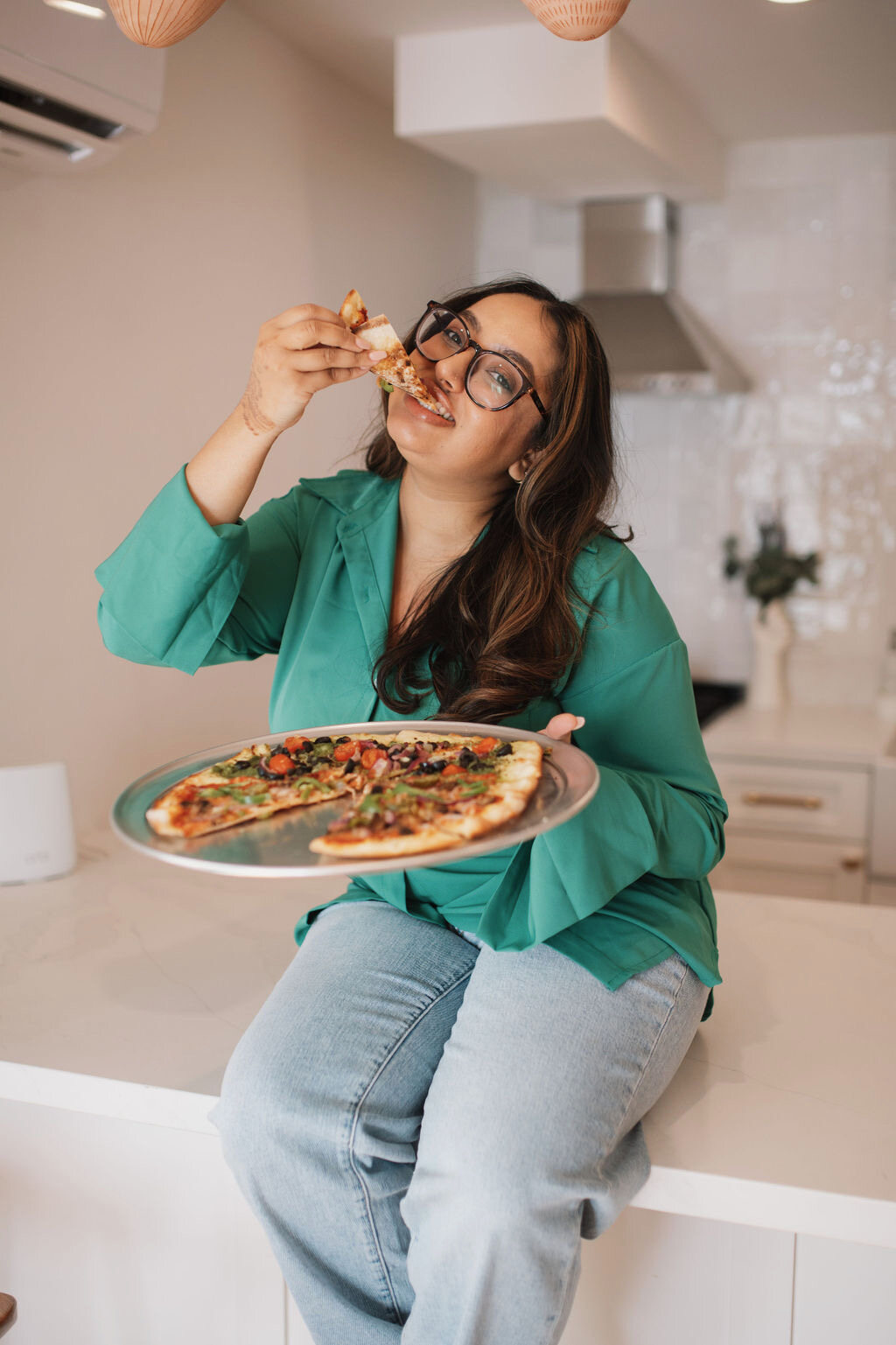 Sheyna Patel holding a slice of pizza in her kitchen